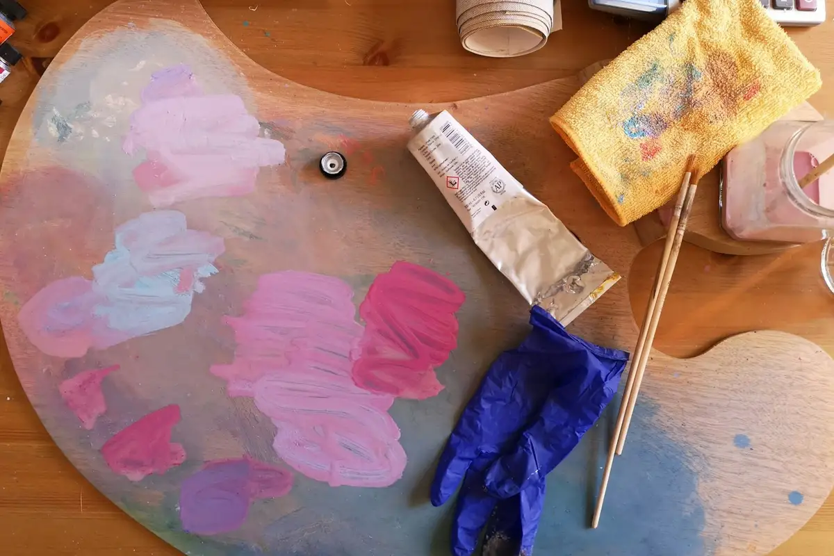 Paleta com misturas de rosa e lilás junto a tubos de tinta e pincéis – Totenart